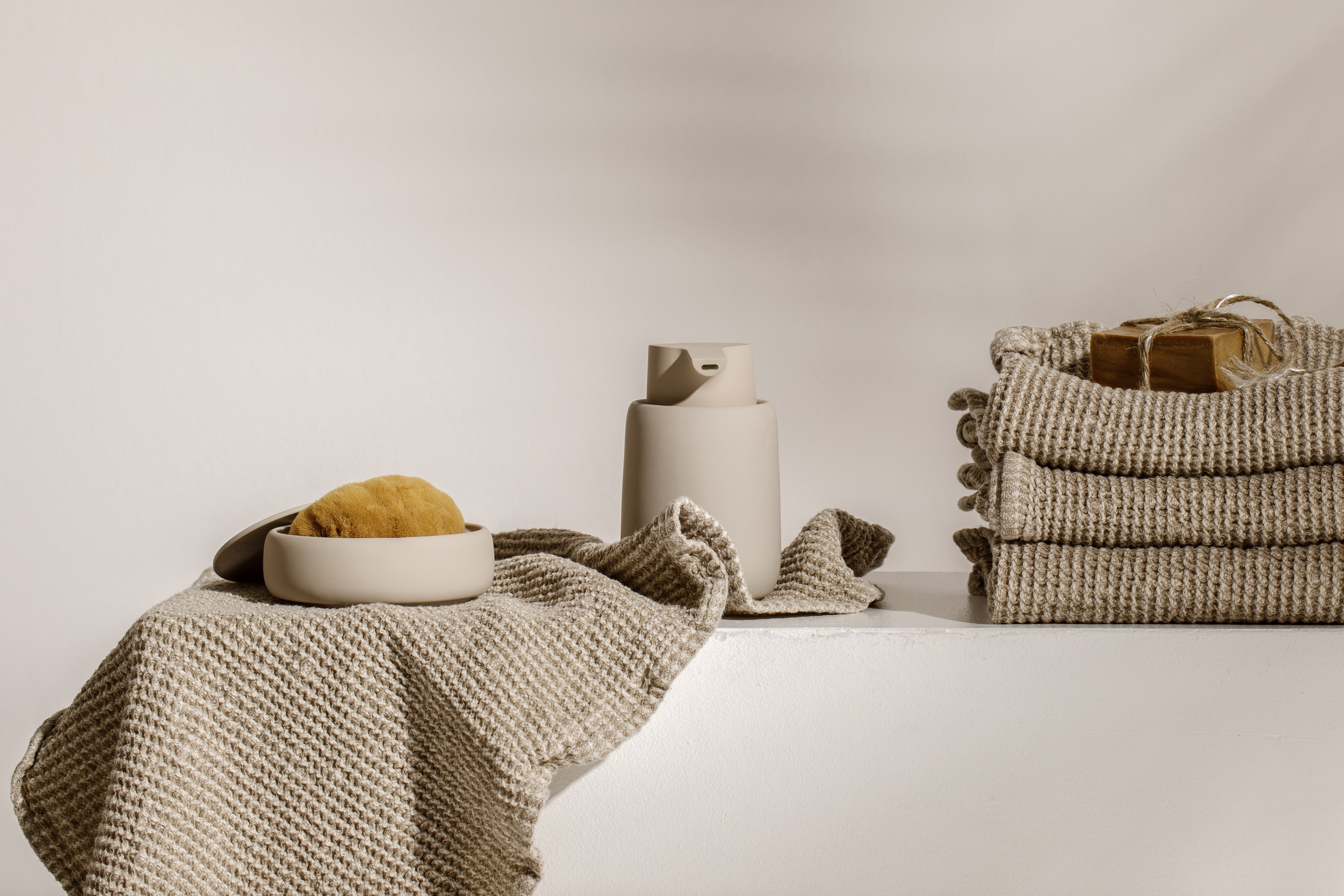 Folded waffle linen towels, natural sponge and a ceramic bowl in warm neutral tones